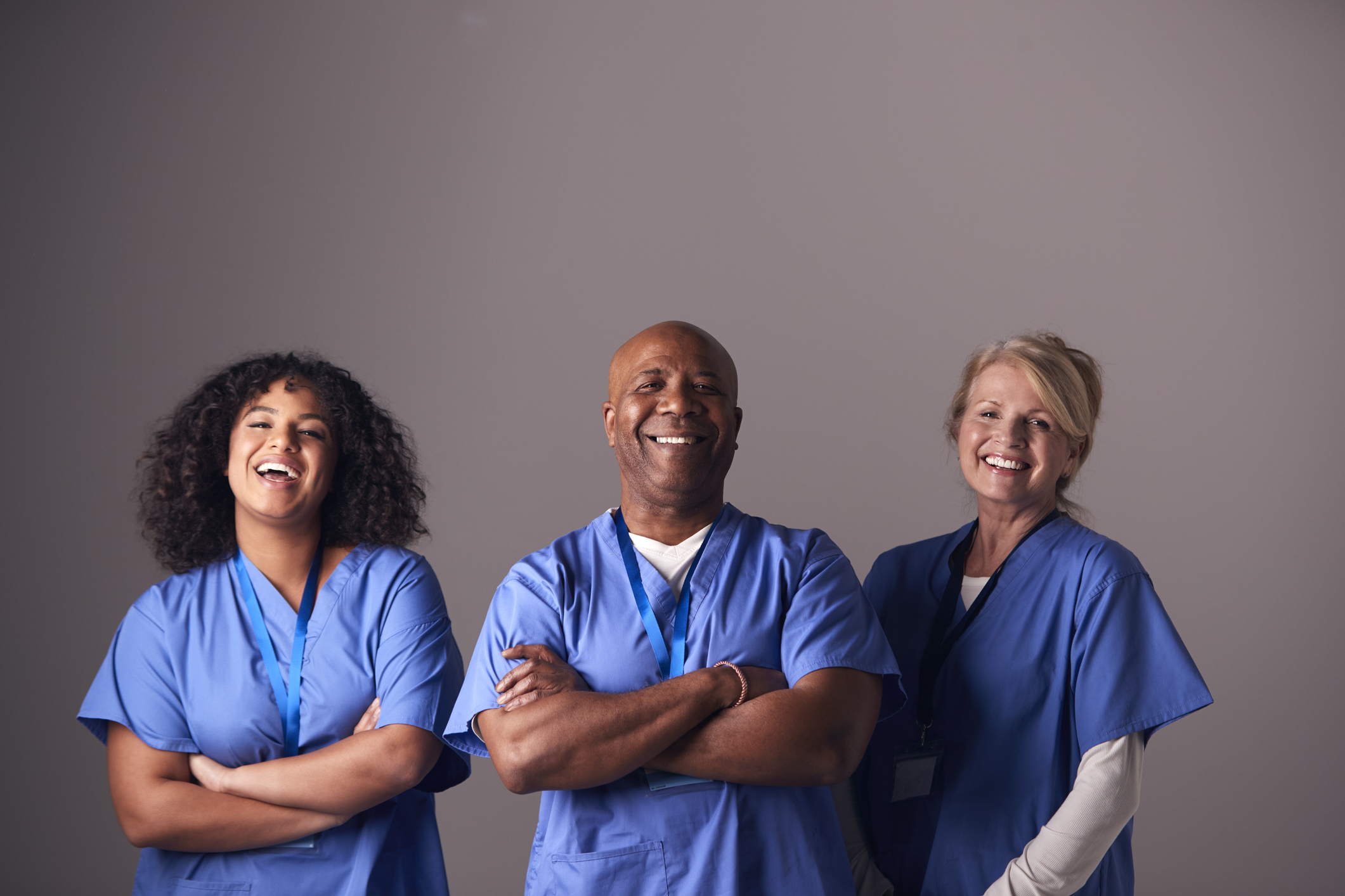 Studio Portrait Of Three Members Of Surgical Team Wearing Scrubs Standing Against Grey Background