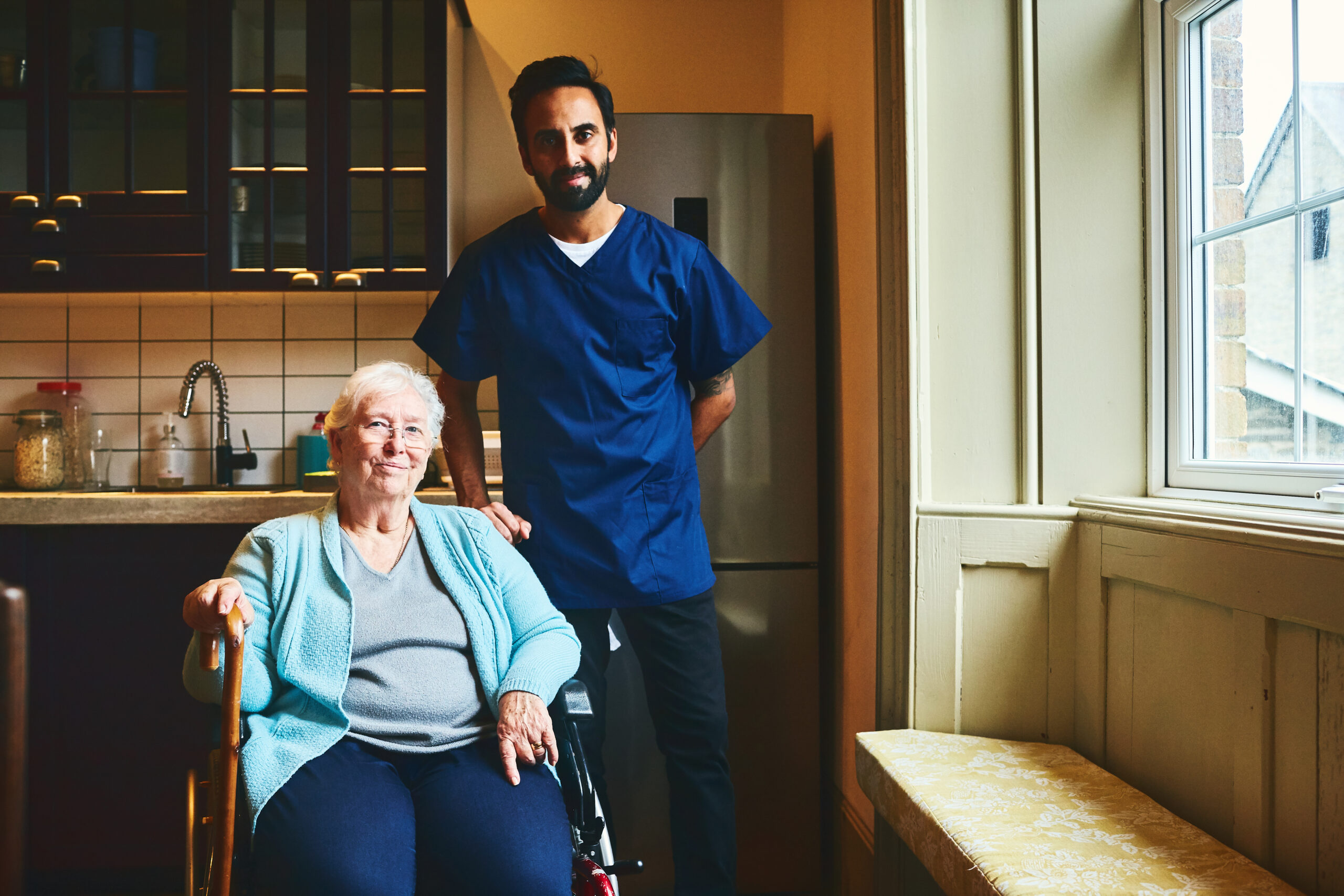 Happy senior woman sitting on wheelchair with male home caregiver standing by